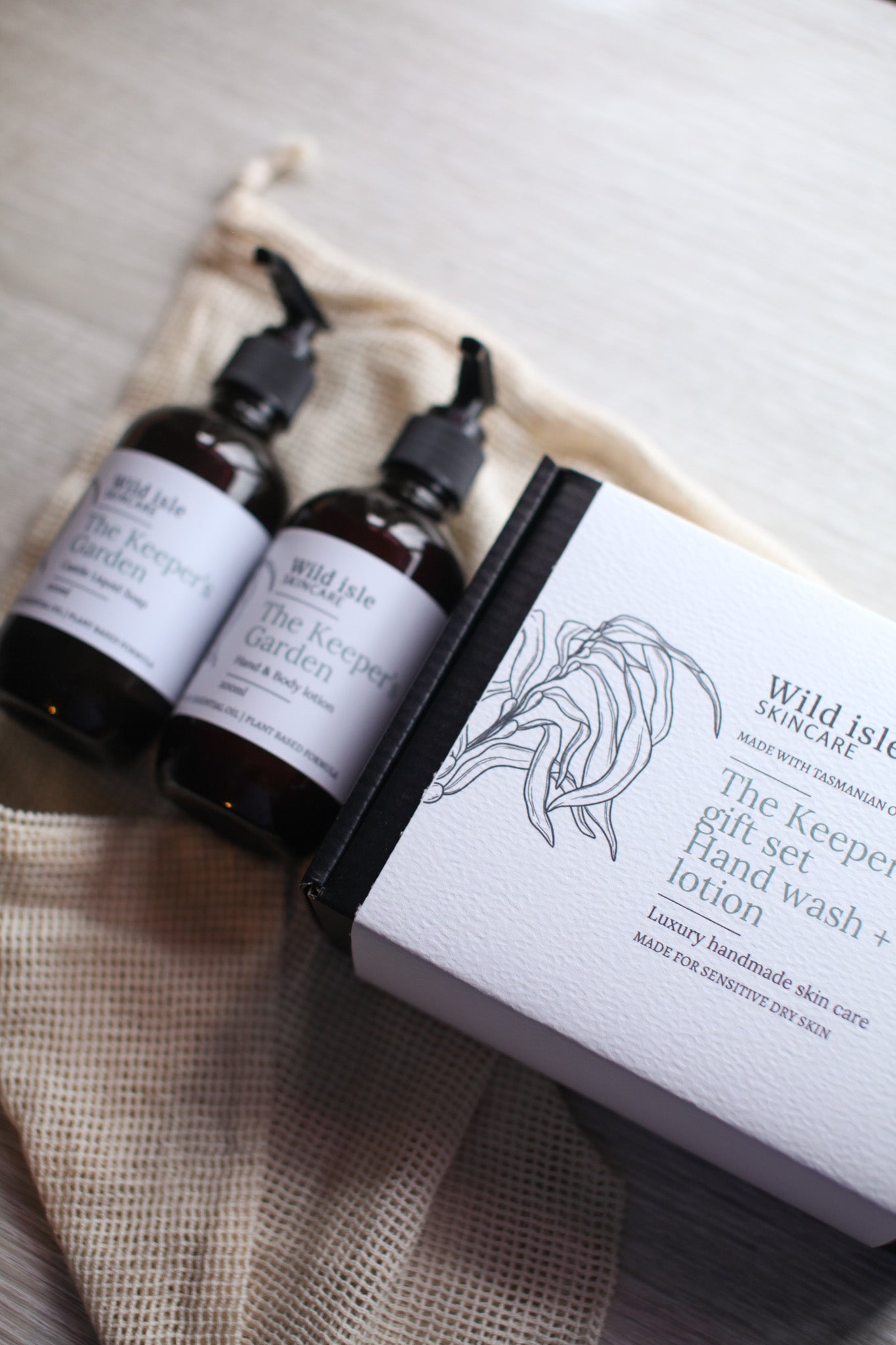 Two bottles of Wild Isle Organics hand wash and lotion with a packaging box on a textured surface.