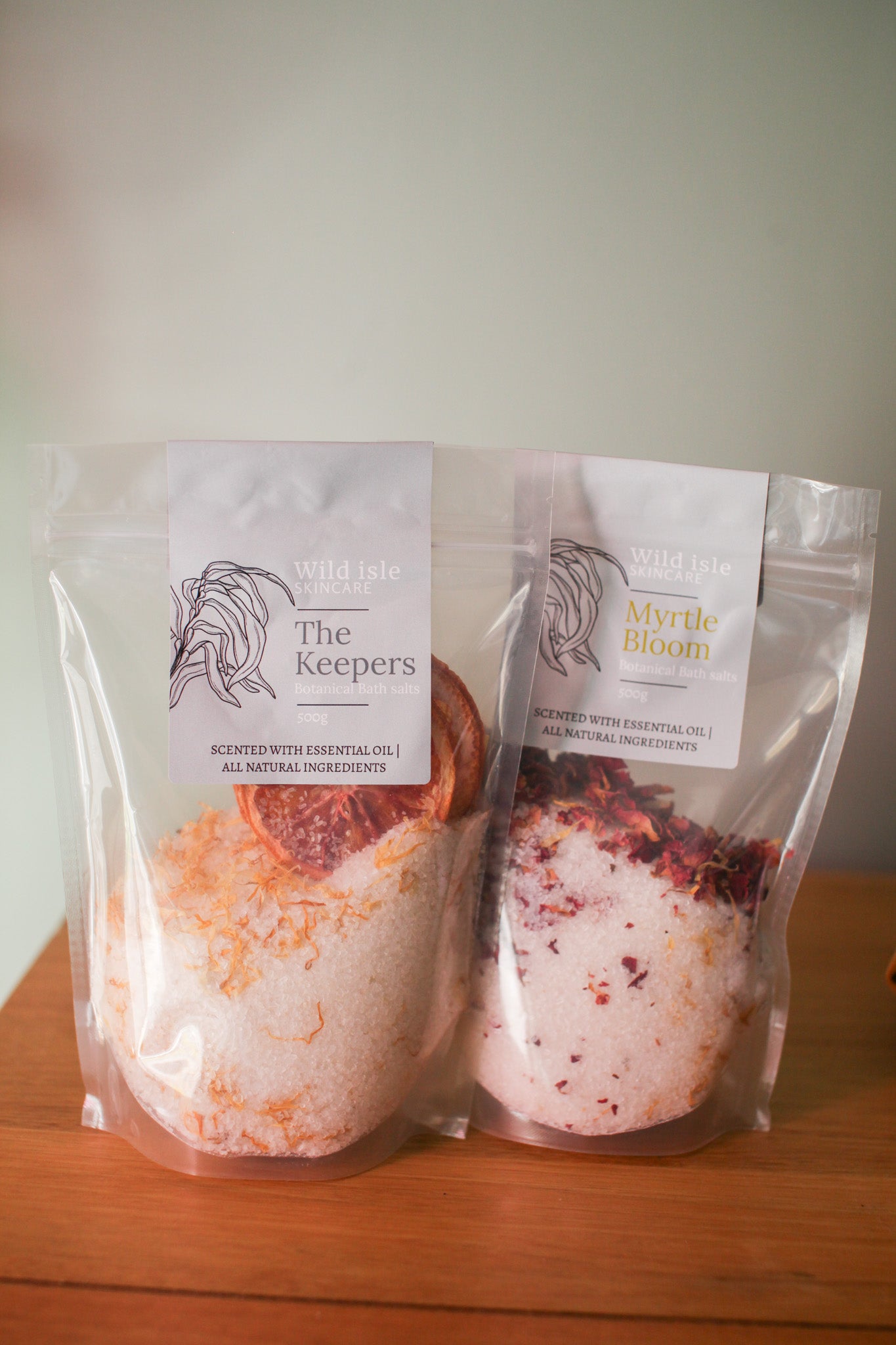 Two bath bombs in clear packaging with 'The Keepers' branding on a wooden surface.