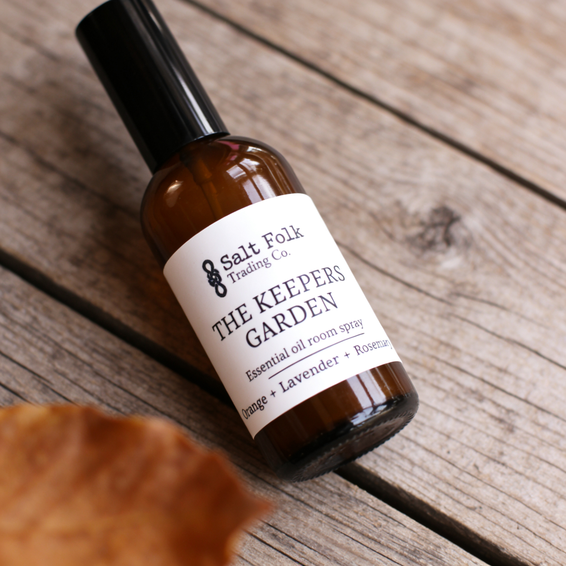 Bottle of 'The Keepers Garden' essential oil room spray by Salt Folk Trading Co. on a wooden surface.